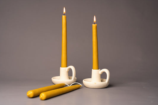 Two lit yellow candles in white ceramic holders on a gray background